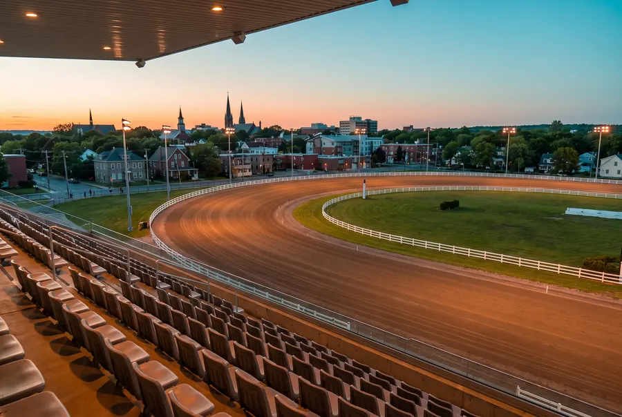 Generated scene: an empty harness racing oval at dusk seen from a grandstand, with a small city and church spires beyond; not a photograph of the racetrack.